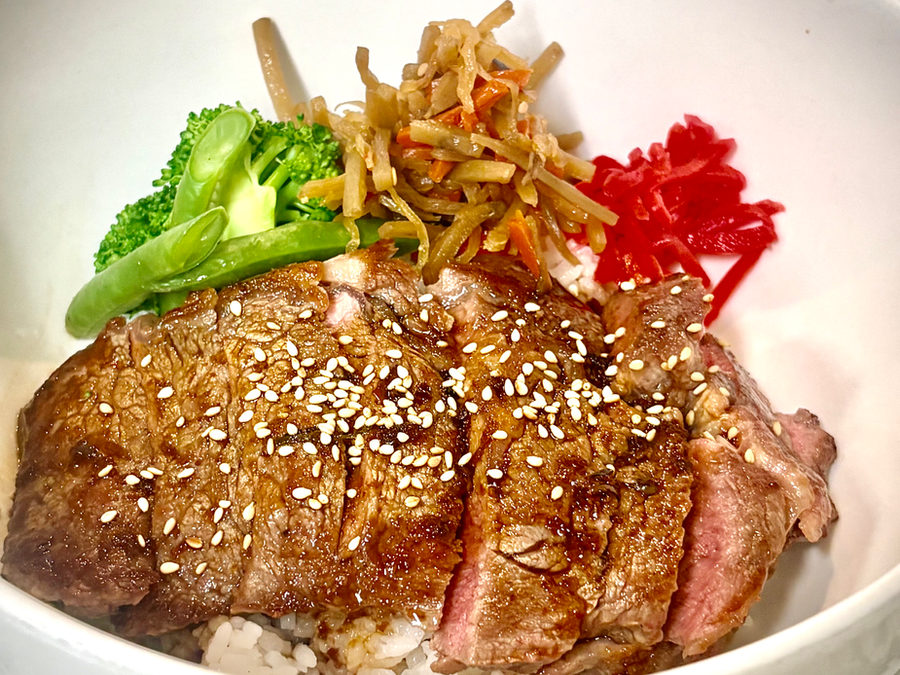 Beef steak donburi bowl with sliced grilled steak, sesame, vegetables and rice